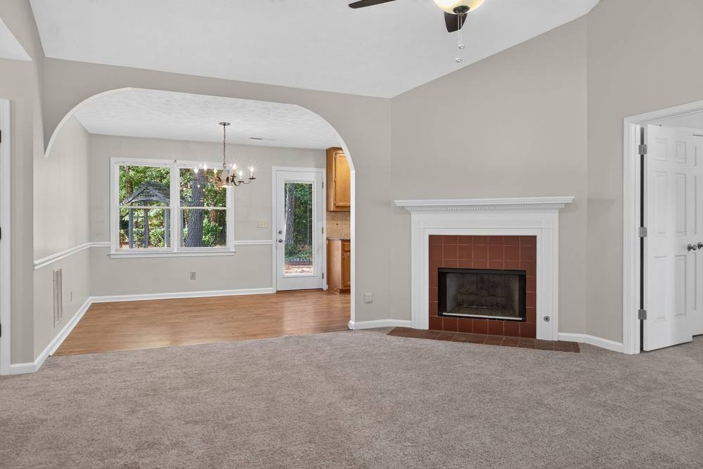 Vaulted living room with corner fireplace and archway to dining area, real estate photography in Covington, GA